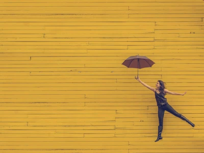 woman holding umbrella jumping against yellow background